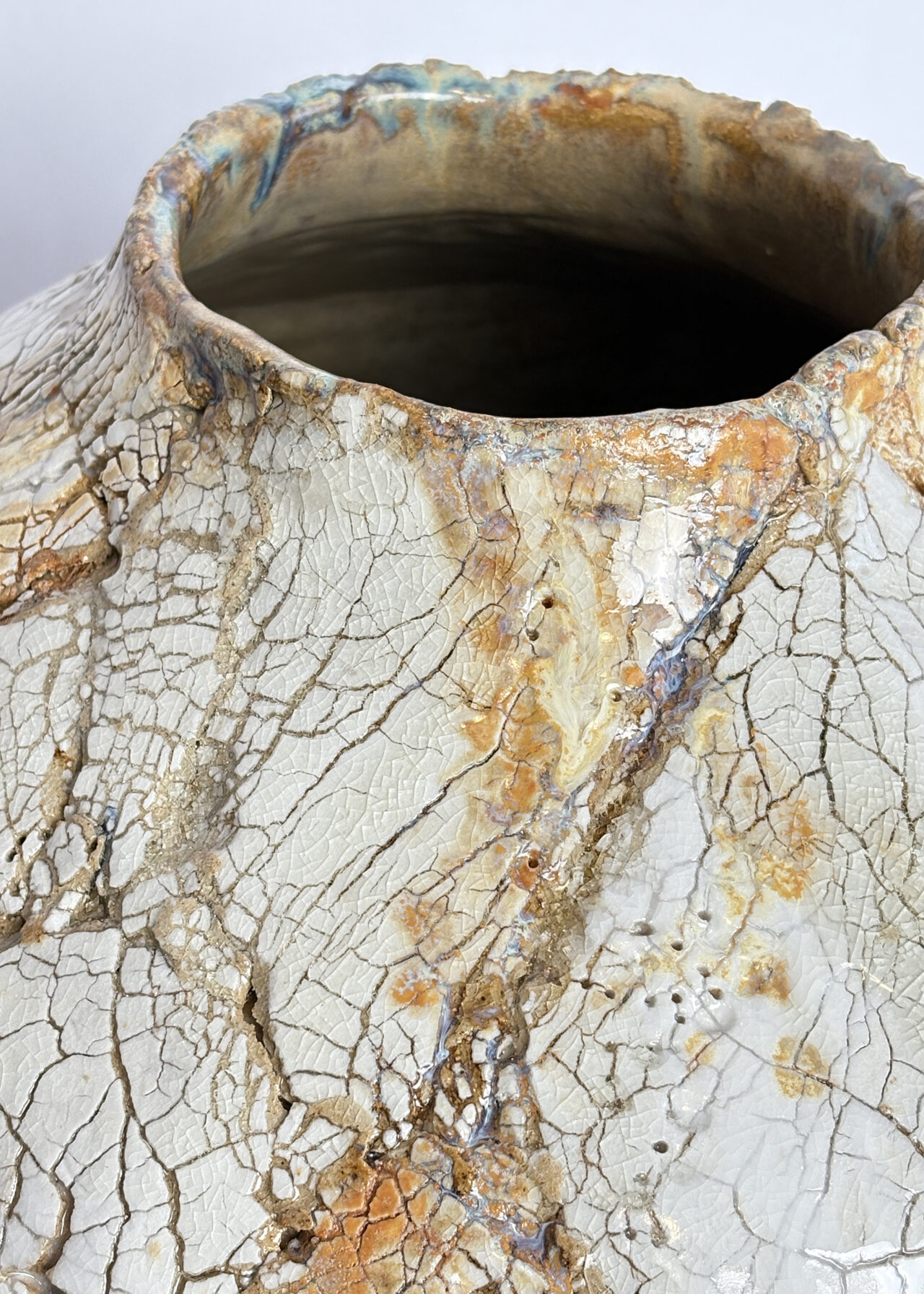 Closeup of the texture from a handbuilt ceramic vessel with cracked textured surface and layered glaze