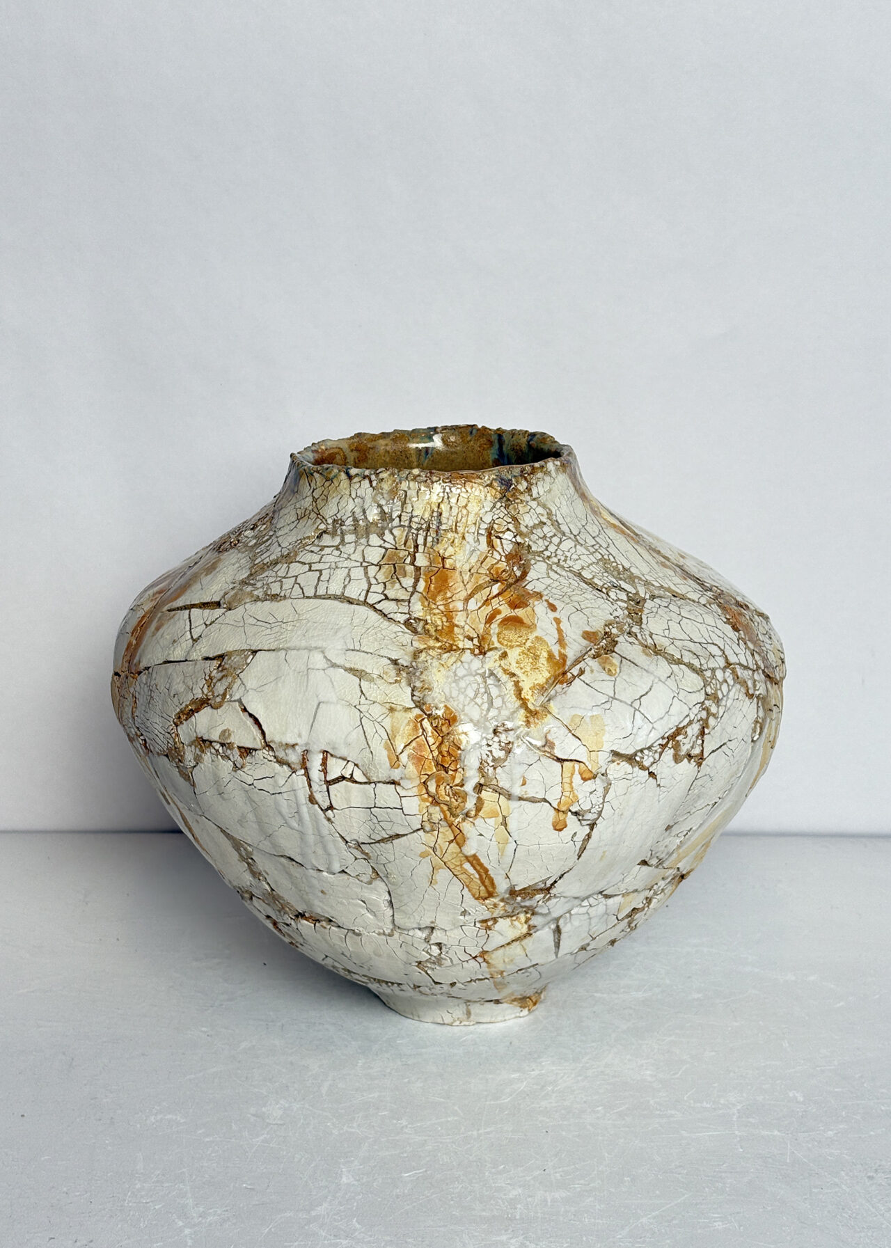 Handbuilt ceramic vessel with cracked textured surface and layered glaze