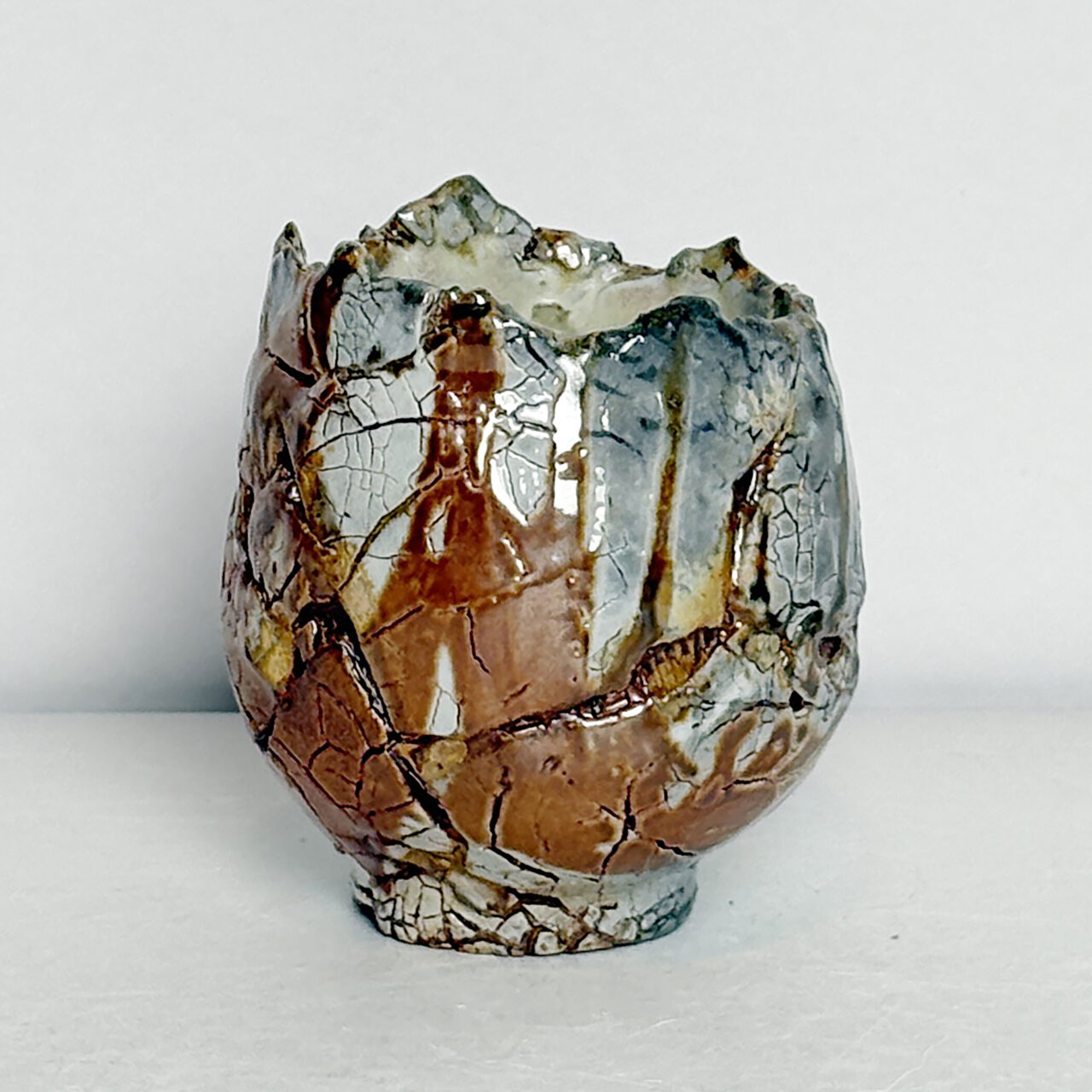 no. 75 Soda fired small ceramic vessel with glossy glaze, crackled surface, and layered rust, white, and blue-gray patches