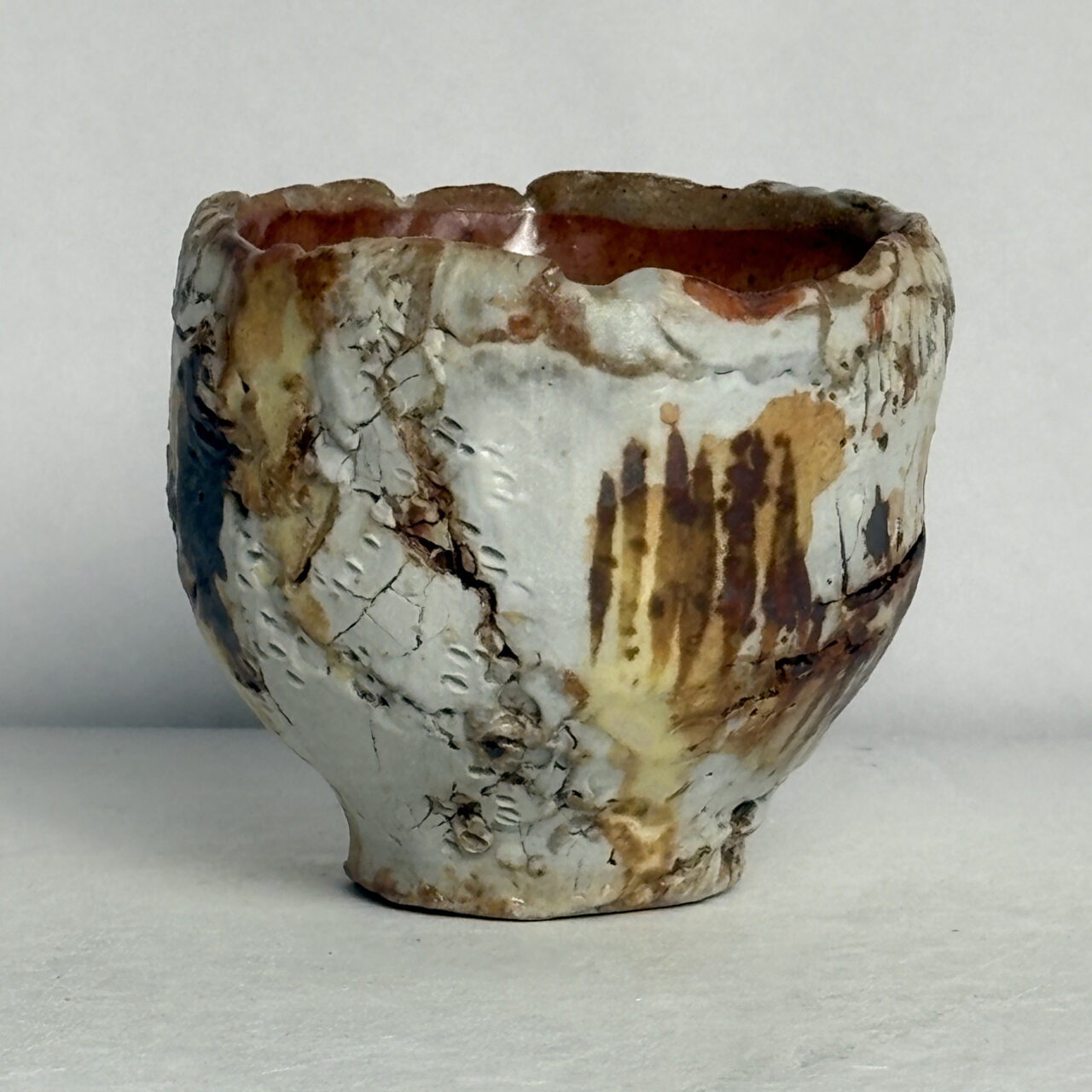 No. 98 Small ceramic vessel with layered white glaze, textured and crackled surface, and vertical rust-colored markings with warm brown and pale yellow tones.