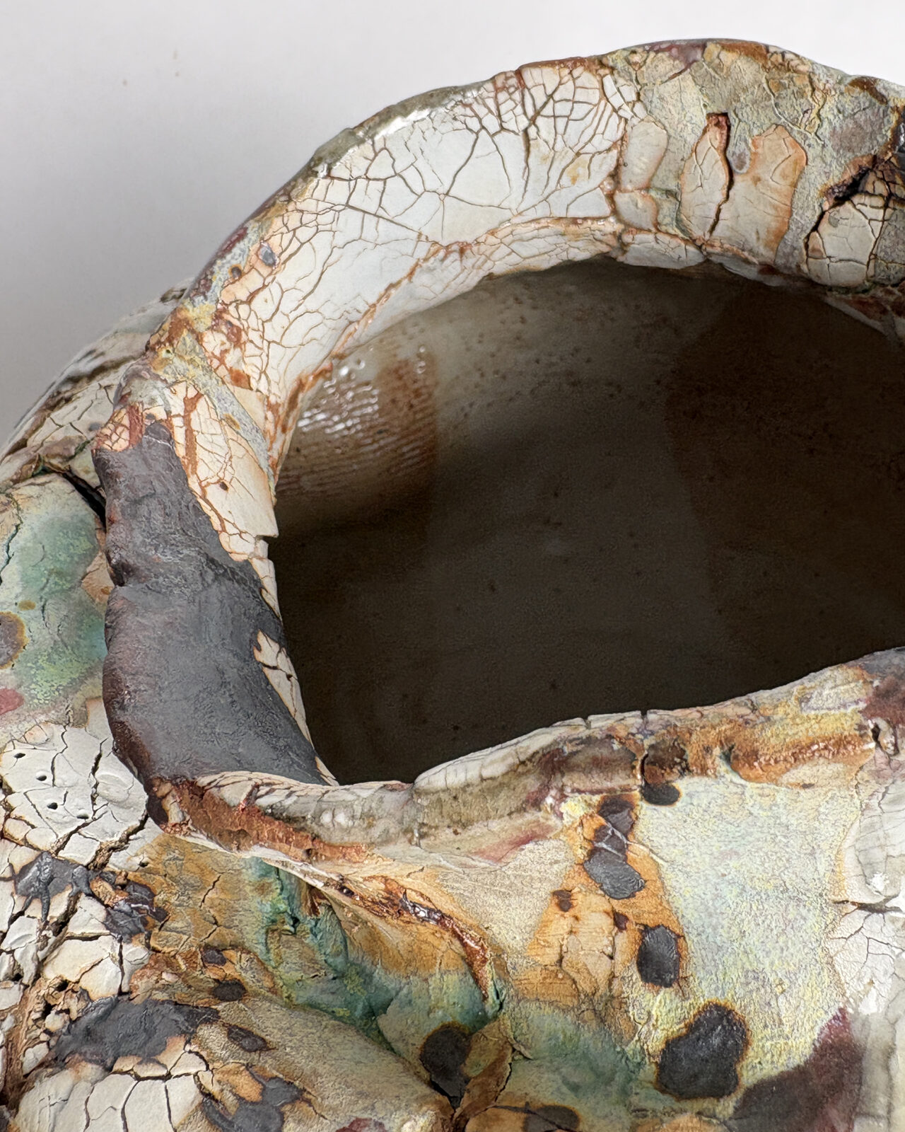 Rim detail of Vessel No. 35 showing uneven sculpted opening, crackled glaze surface, and layered black, rust, and pale green glaze effects.