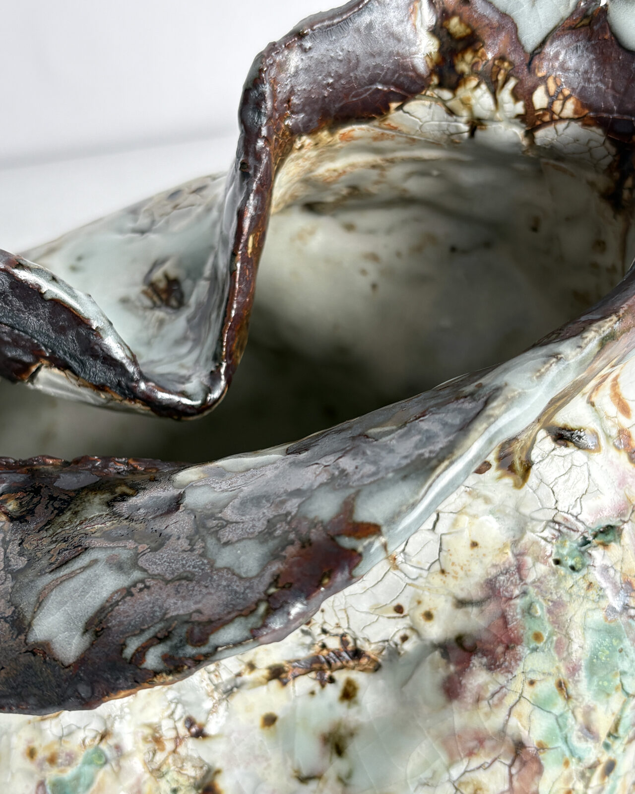 Rim detail of Vessel No. 43 showing folded sculptural opening, dark glossy glaze along the rim, and crackled white and pale green surface texture.