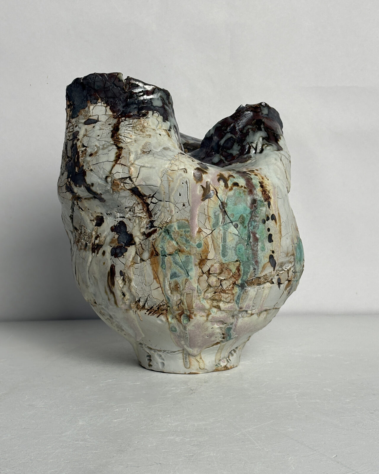 Side view of Vessel No. 43 with rounded asymmetrical form, layered white glaze, pale green washes, and scattered rust and dark brown markings.