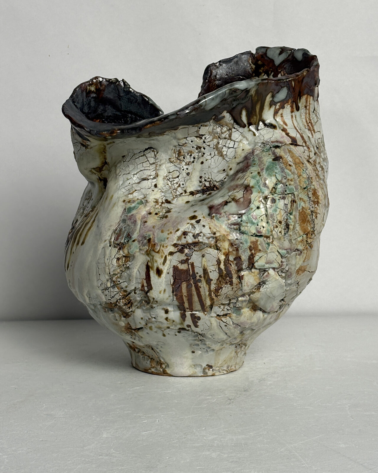 Alternate side view of Vessel No. 43 showing folded rim, crackled white glaze, layered rust-colored markings, and pale green glaze accents across the textured surface.