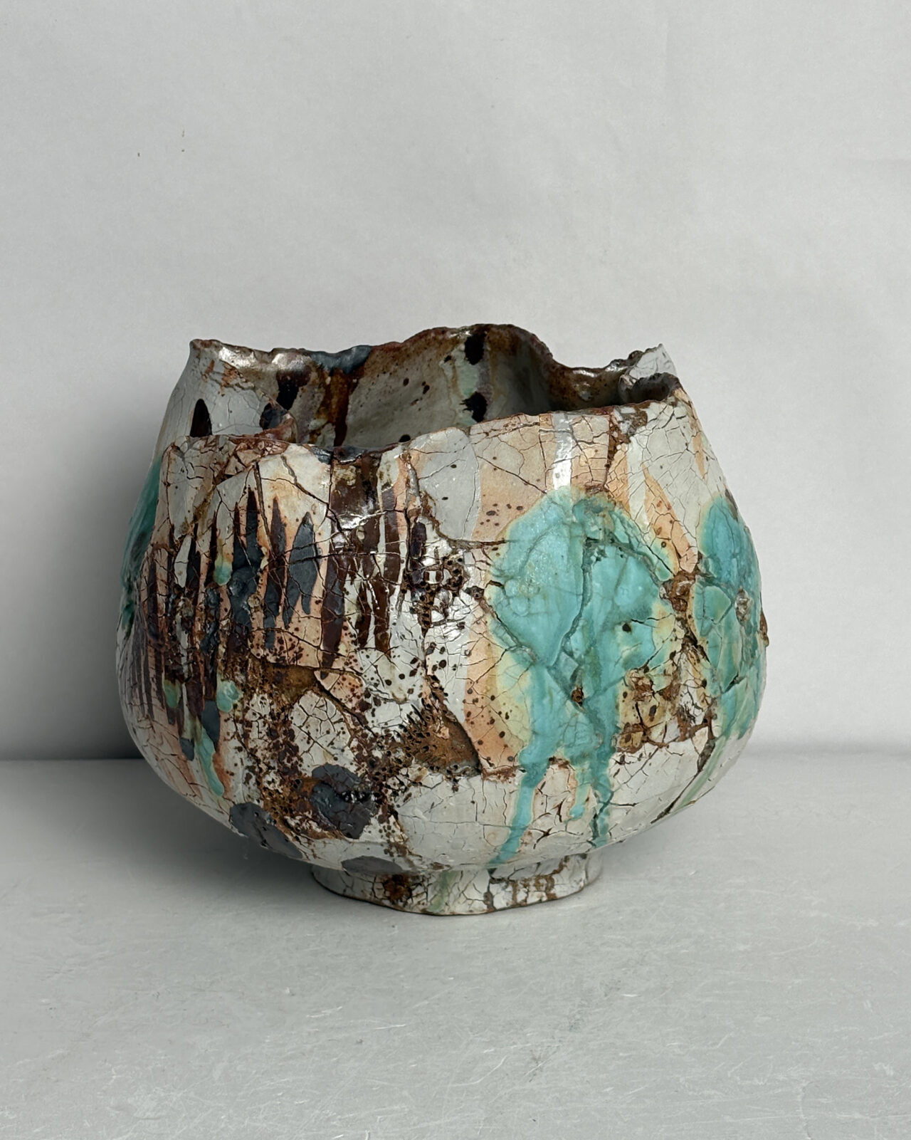 Side view of Vessel No. 57 with rounded form, crackled white glaze, turquoise glaze pools, and layered dark brown linear markings.