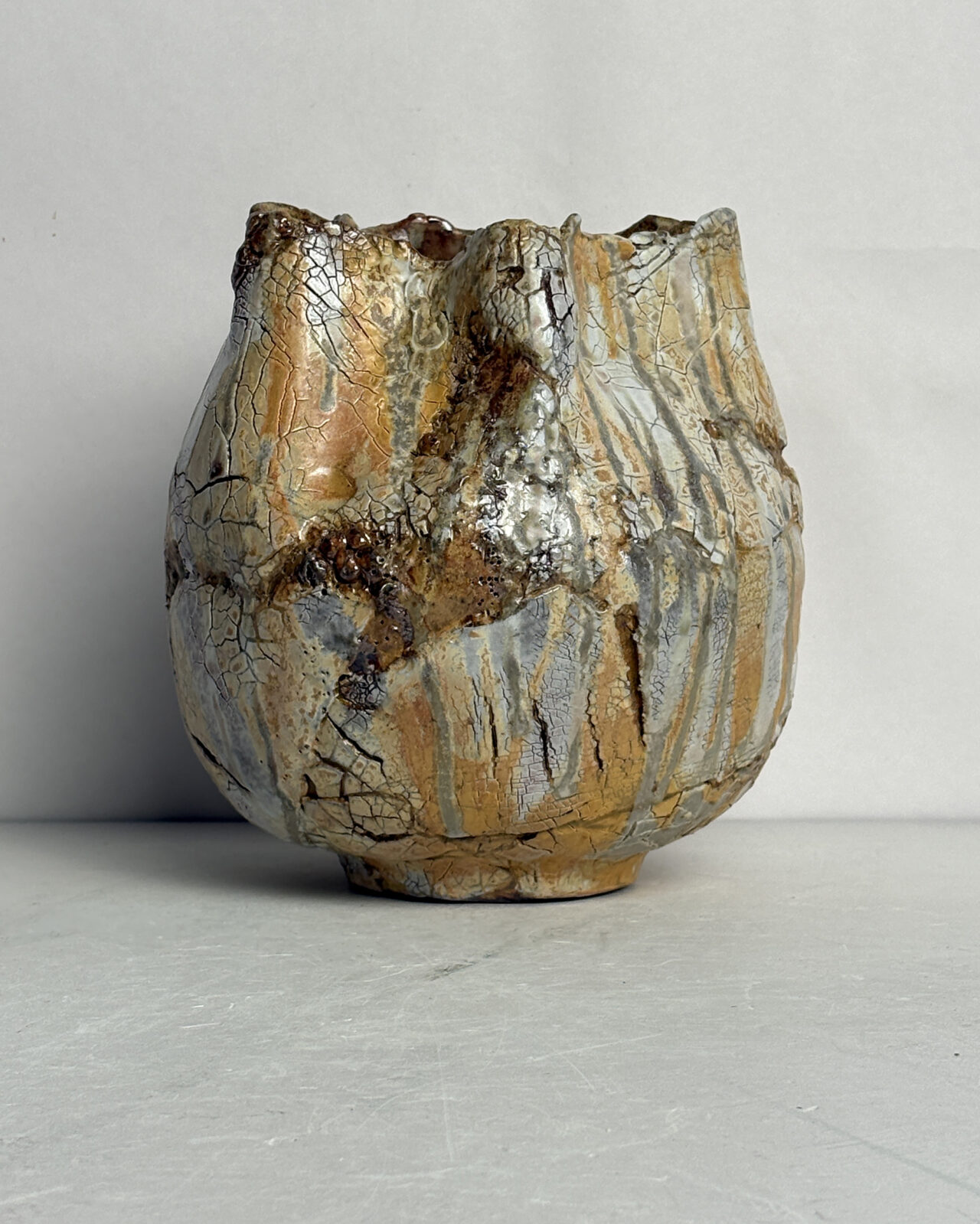 Vessel no. 58, ceramic with a rounded faceted form, irregular rim, and layered surface in ochre, cream, gray, and rust tones with crackled glaze and flowing vertical markings.