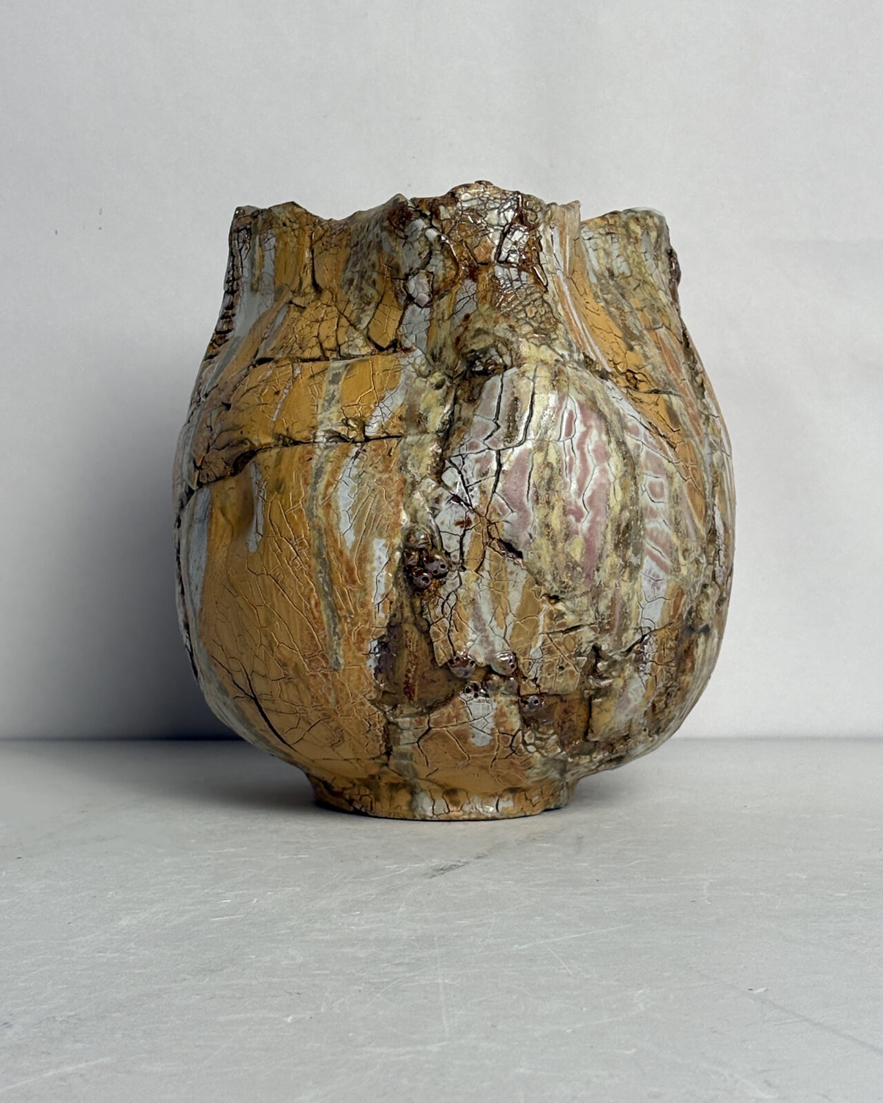 Vessel no. 58 Side view of a soda-fired ceramic vessel with vertically faceted planes, warm ochre and gray flashing, and heavily crackled glaze surfaces.
