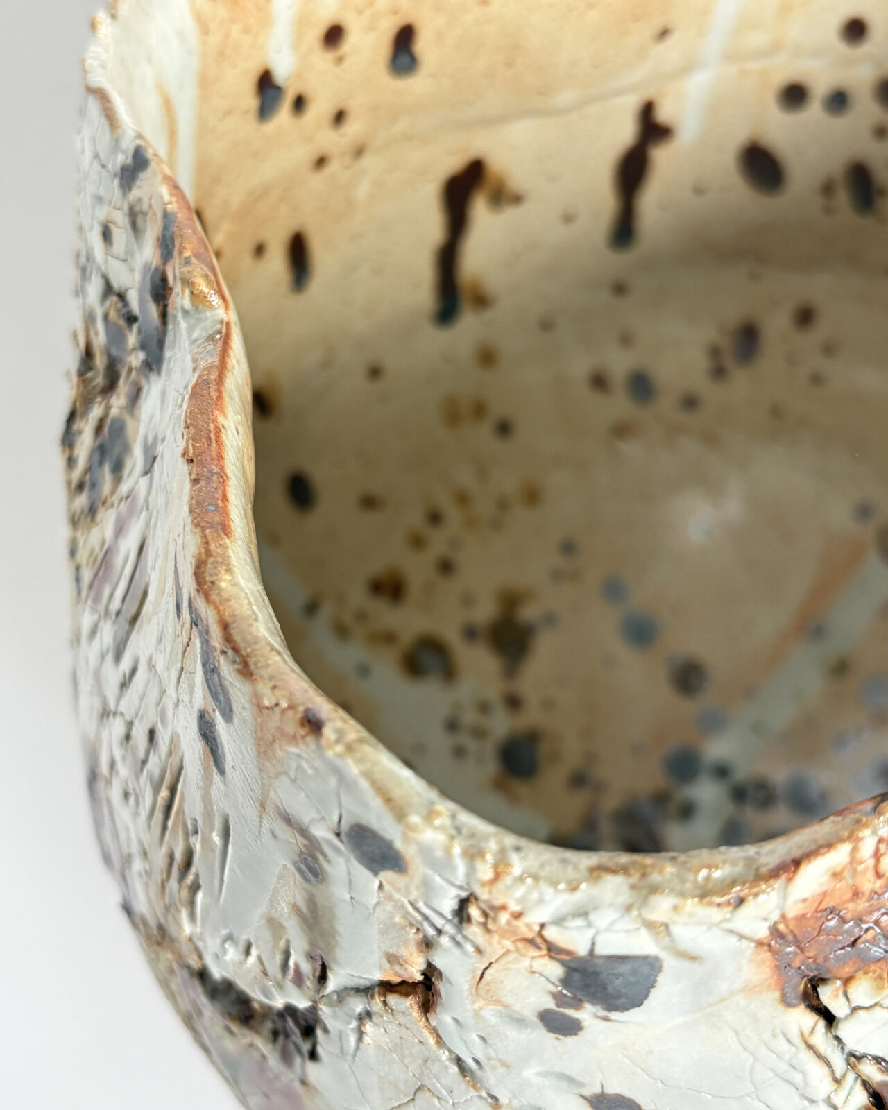 Vessel no. 72 - Rim detail of a ceramic bowl shaped vessel with a fluted edge and rust brown marking on a creamy white textured surface and pale yellow interior,