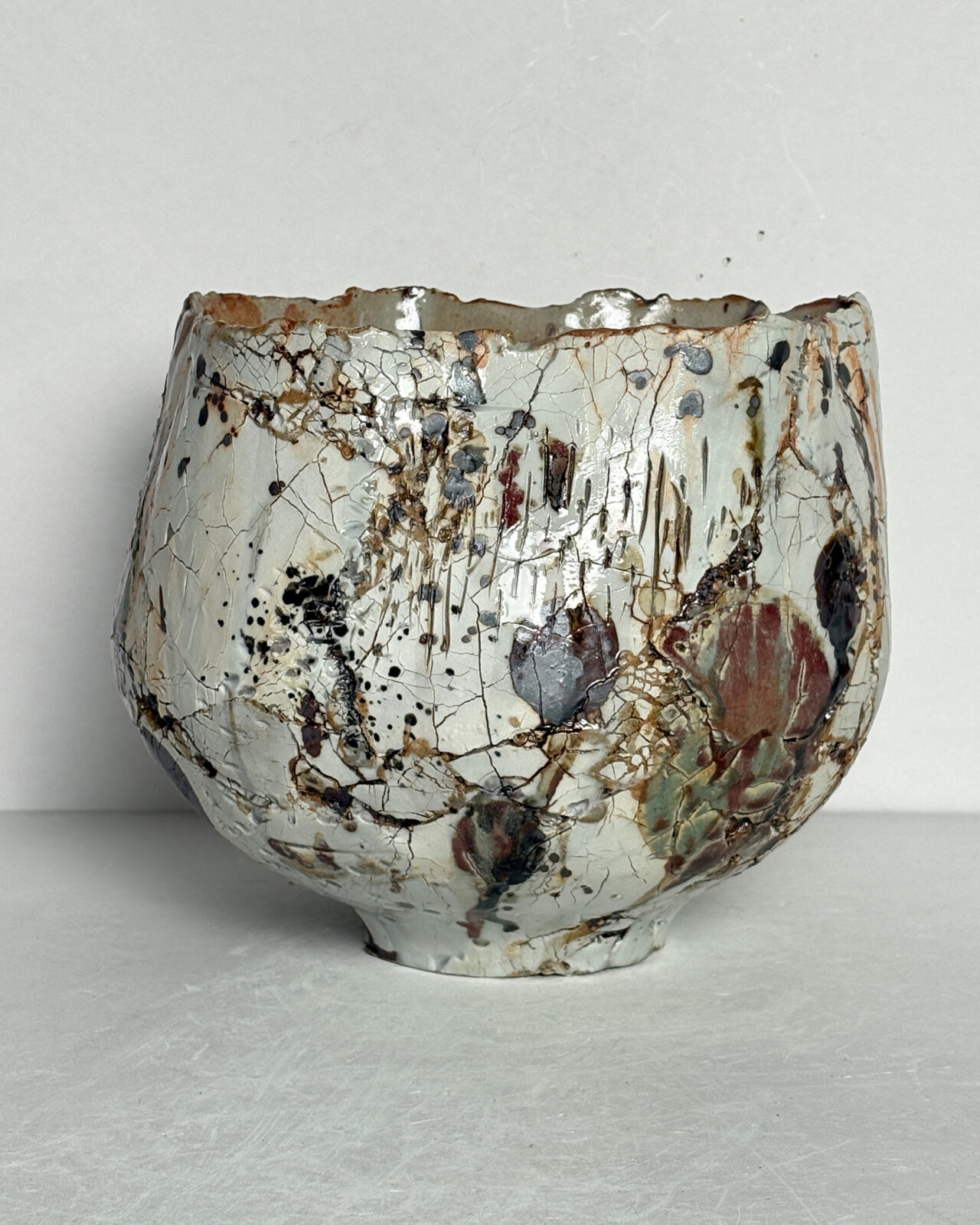 Vessel no. 72 - Side 3 of a ceramic bowl shaped vessel with a fluted edge and rust brown marking on a creamy white textured surface.
