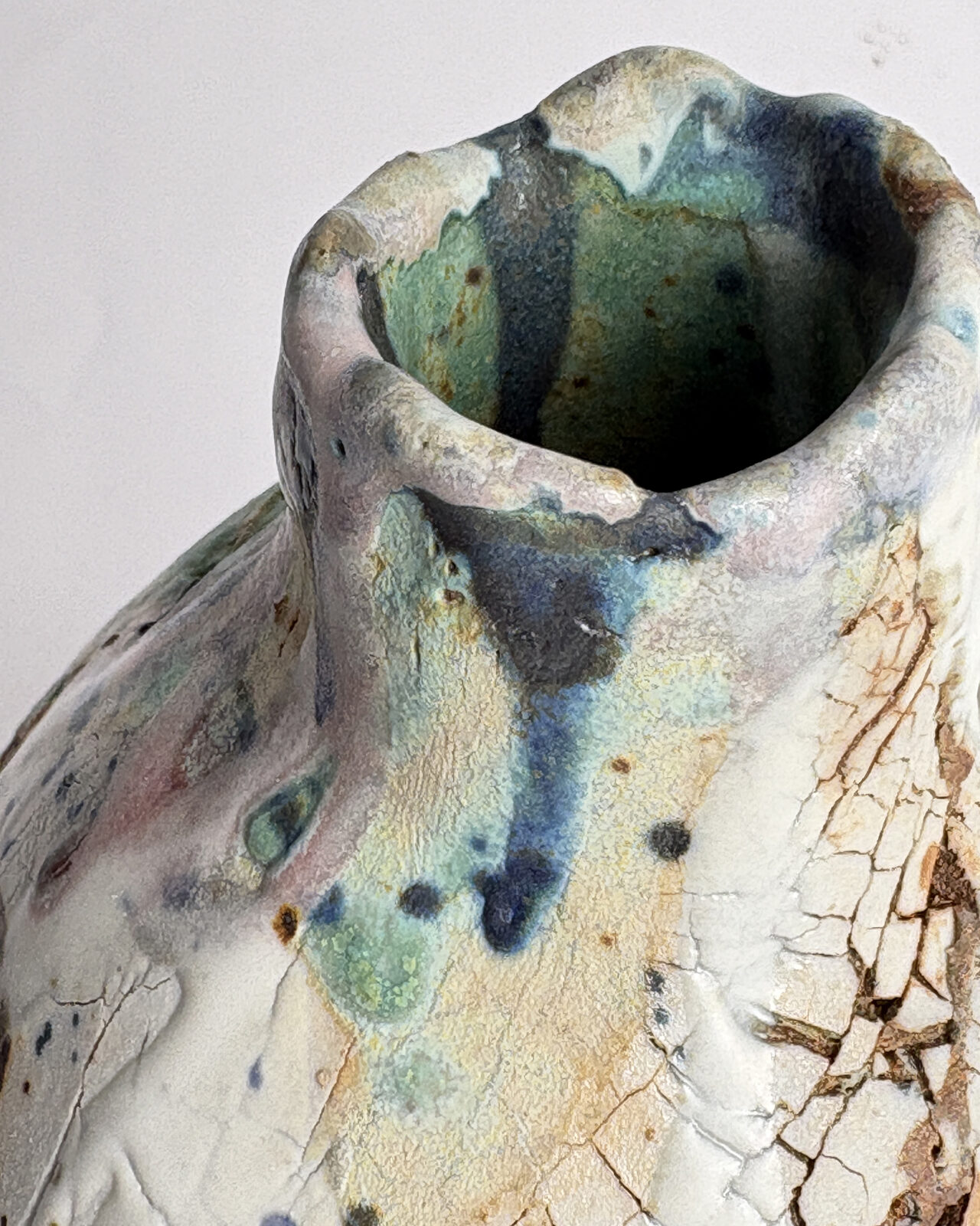 Close-up of the irregular rim of Vessel No. 61 with layered turquoise, blue, and pale pink glazes flowing into a dark green interior.