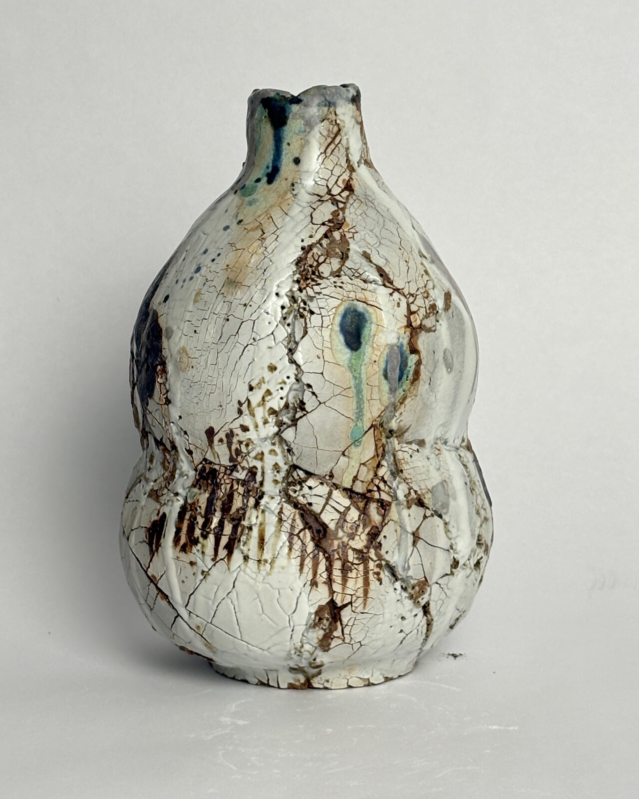 Side view of Vessel No. 61 showing a cracked white ceramic surface with rust-colored fissures and turquoise and blue glaze markings.