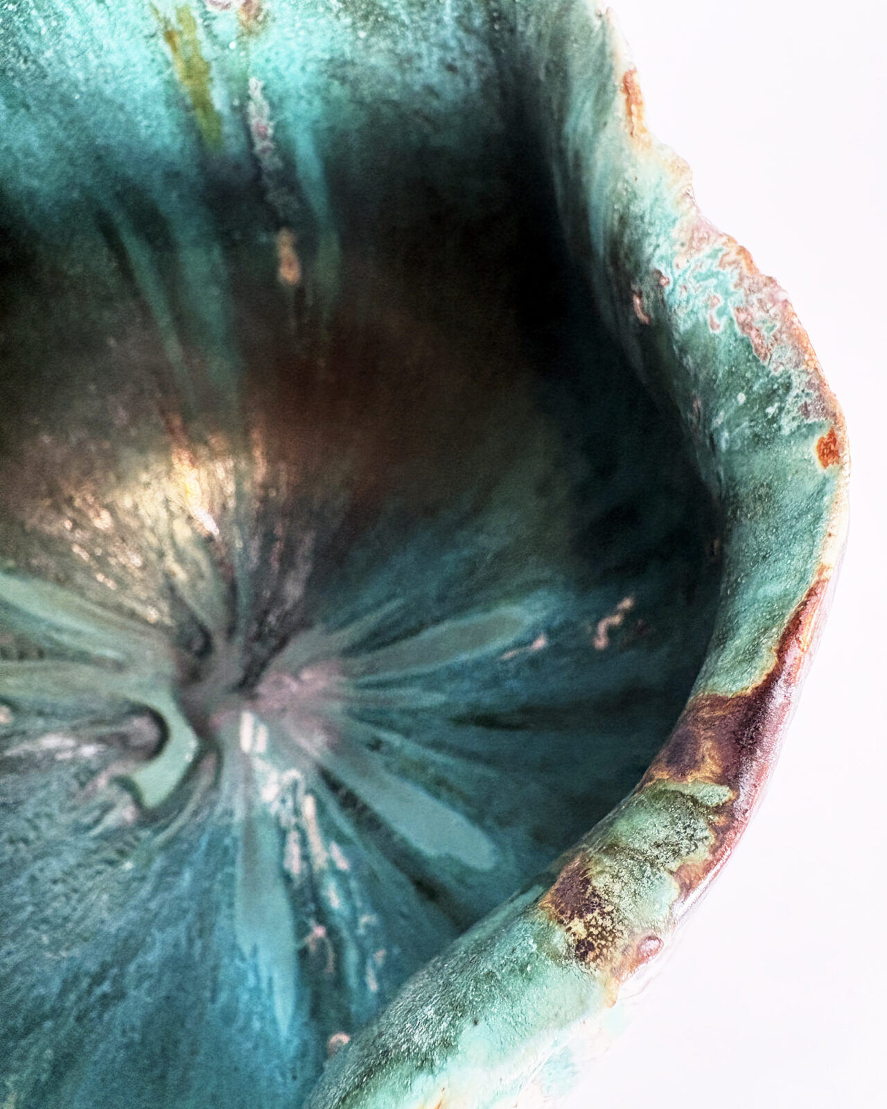 Overhead detail of a ceramic vessel's irregular rim and glossy emerald green interior, with swirling turquoise glazes and subtle reddish-brown accents.