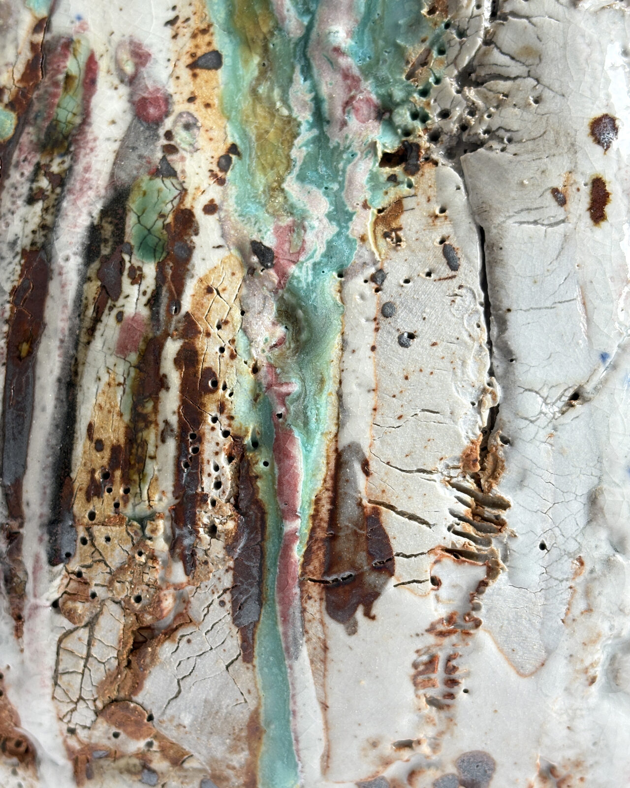 Extreme close-up of a ceramic surface showing cracked porcelain slip, pitted clay, flowing turquoise and pink glazes, and rust-colored iron oxide markings.