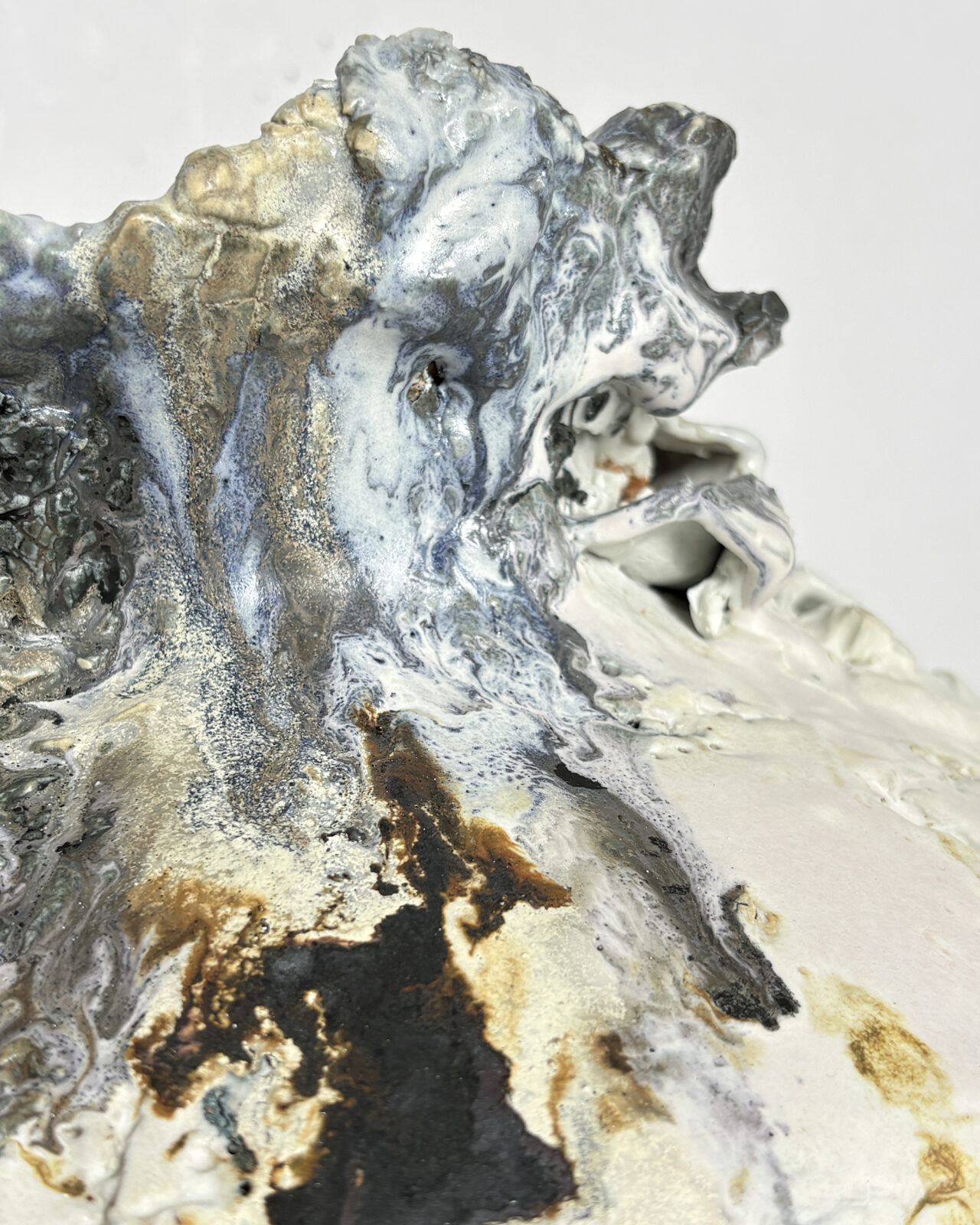 Close-up of an irregular ceramic vessel rim with sculptural clay formations, folded edges, and swirling gray, cream, and pale blue glazes.
