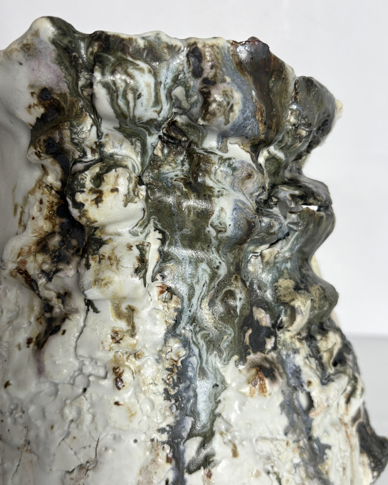 Close-up of a sculptural ceramic vessel with fractured white porcelain slip, warm ochre markings, flowing charcoal-gray glazes, and a heavily textured, irregular rim.